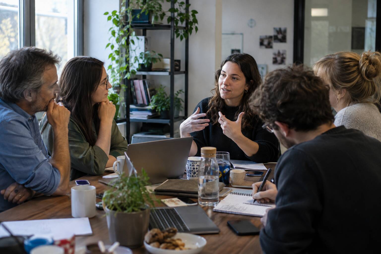 Cinq personnes sont assises autour d'une table dans un bureau et discutent